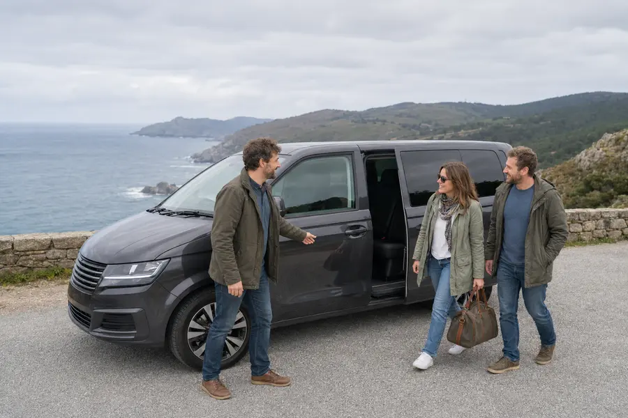Conductor recibiendo a viajeros junto a un vehículo privado en la costa gallega