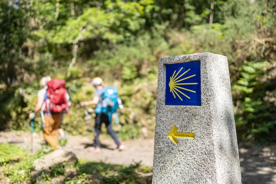 Peregrinos caminando junto a un mojón del Camino de Santiago